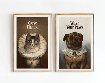 May include: Two framed prints with vintage illustrations of a cat and a dog. The cat is wearing a white lace collar and the text "Close The Lid" is above it. The dog is wearing a white lace collar and the text "Wash Your Paws" is above it.