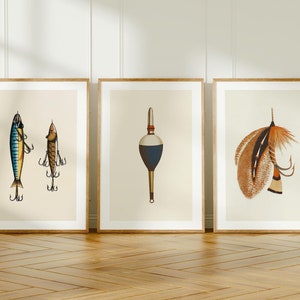May include: Three framed prints of vintage fishing lures. The first print features two lures, one blue and yellow and the other gold and brown. The second print features a red and blue bobber. The third print features a brown and orange feathered lure.