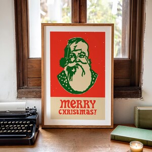 Op de afbeelding: Een ingelijste poster met een rode achtergrond waarop een cartoonillustratie van de kerstman met een groene hoed en baard te zien is. De tekst "merry christmas!" is in groen en wit onder de illustratie gedrukt.