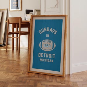 Peut inclure: Une impression encadr&eacute;e avec un fond bleu et du texte blanc qui dit "Sundays in 1934 Detroit Michigan". Un ballon de football blanc avec le num&eacute;ro "1934" est centr&eacute; sur l'impression.