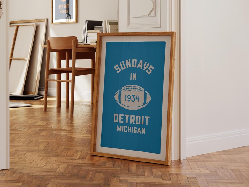 Peut inclure: Une impression encadr&eacute;e avec un fond bleu et du texte blanc qui dit "Sundays in 1934 Detroit Michigan". Un ballon de football blanc avec le num&eacute;ro "1934" est centr&eacute; sur l'impression.