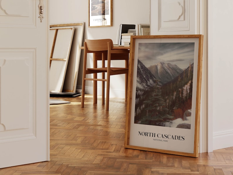 K&ouml;nnte beinhalten: Ein gerahmtes Poster mit einem Foto einer Bergkette mit schneebedeckten Gipfeln und einem Wald im Vordergrund. Das Poster tr&auml;gt den Titel "North Cascades National Park".