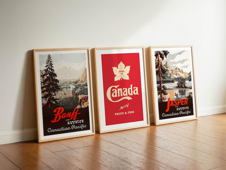 Op de afbeelding: Drie ingelijste reisposters leunen tegen een witte muur. De posters tonen vintage ontwerpen met de teksten "Banff", "Canada" en "Jasper". De "Canada" poster heeft een rode achtergrond met een esdoornblad.