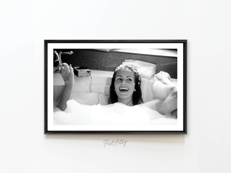 Peut inclure: Une photographie en noir et blanc d'une femme dans un bain moussant, souriante et &eacute;coutant de la musique. Elle porte une serviette blanche et a les cheveux tir&eacute;s en arri&egrave;re. Le bain est rempli de bulles.
