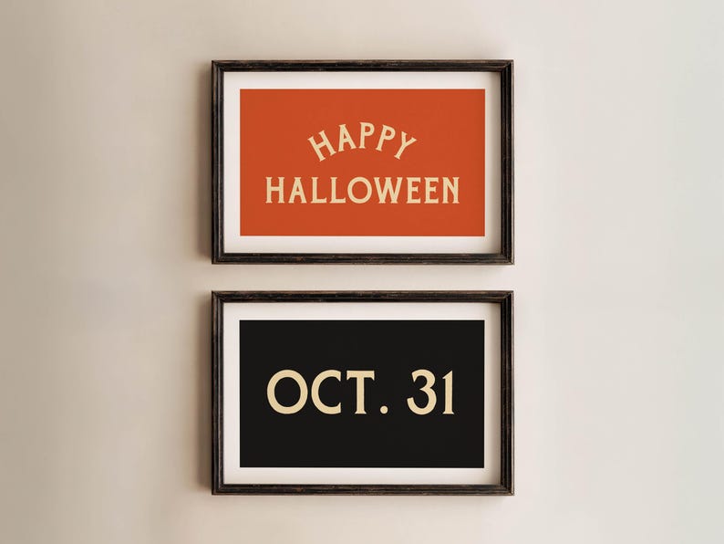May include: Two framed Halloween-themed prints. The top print has an orange background with "HAPPY HALLOWEEN" in cream-colored text. The bottom print has a black background with "OCT. 31" in cream-colored text. Both are in dark brown frames.