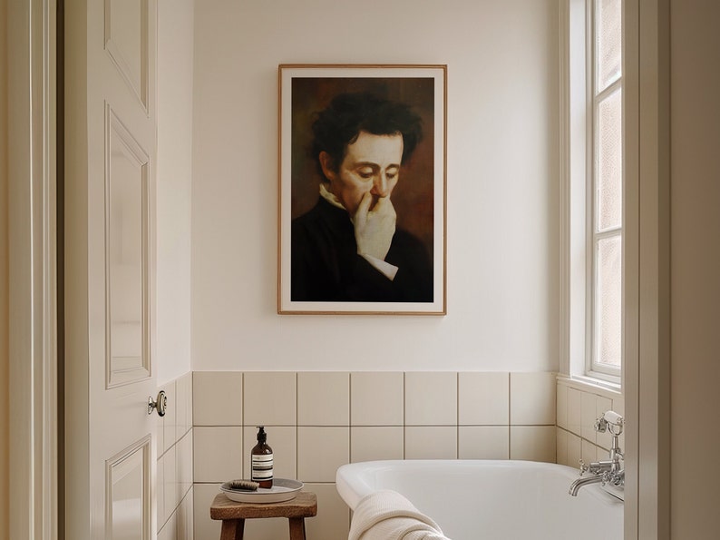 Op de afbeelding: Een ingelijst portret van een man in een donker pak met een witte handschoen die zijn mond bedekt. Het portret hangt aan een witte muur in een badkamer met een wit bad en witte tegels.