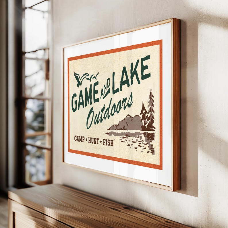 Op de afbeelding: Een vintage poster met een bruin, oranje en wit kleurenschema. De poster toont de tekst "GAME AND LAKE Outdoors CAMP HUNT FISH" met een gestileerde afbeelding van een meer en bomen.