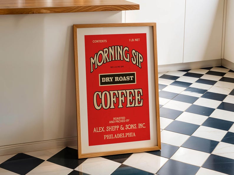 May include: A framed vintage coffee advert in red and cream. The text reads "MORNING SIP DRY ROAST COFFEE" with "ALEX. SHEPP & SONS, INC. PHILADELPHIA" at the bottom. The frame is light brown. The image is leaning against a wall.