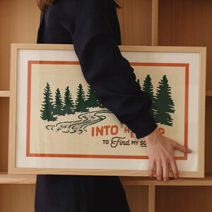 Puede incluir: Una impresi&oacute;n enmarcada con una est&eacute;tica vintage que presenta una escena de bosque verde con un r&iacute;o sinuoso y el texto "Into the Wild to Find My Soul".