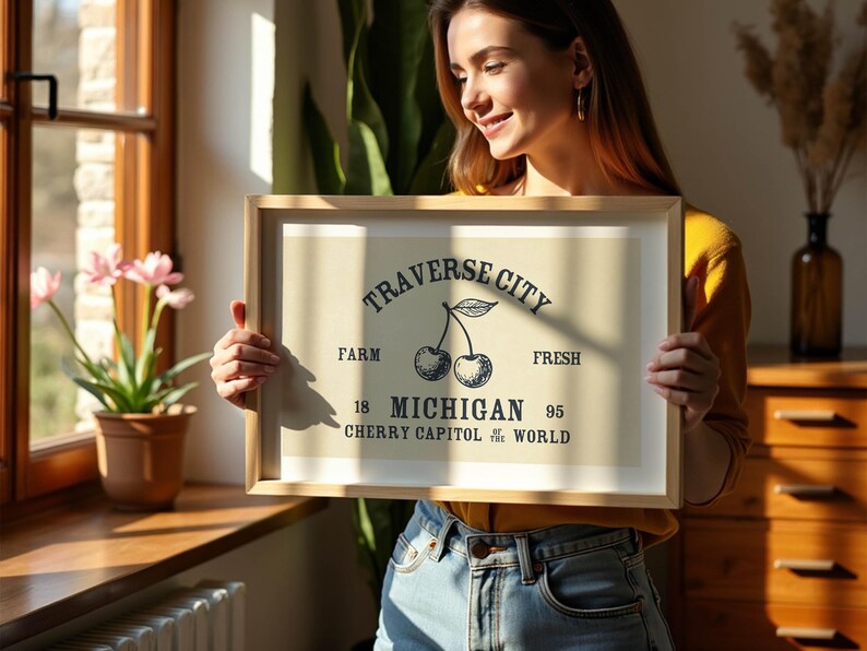 May include: A framed print with a light beige background featuring a black illustration of two cherries and text that reads "Traverse City Farm Fresh Michigan Cherry Capitol of the World". The frame is light brown.
