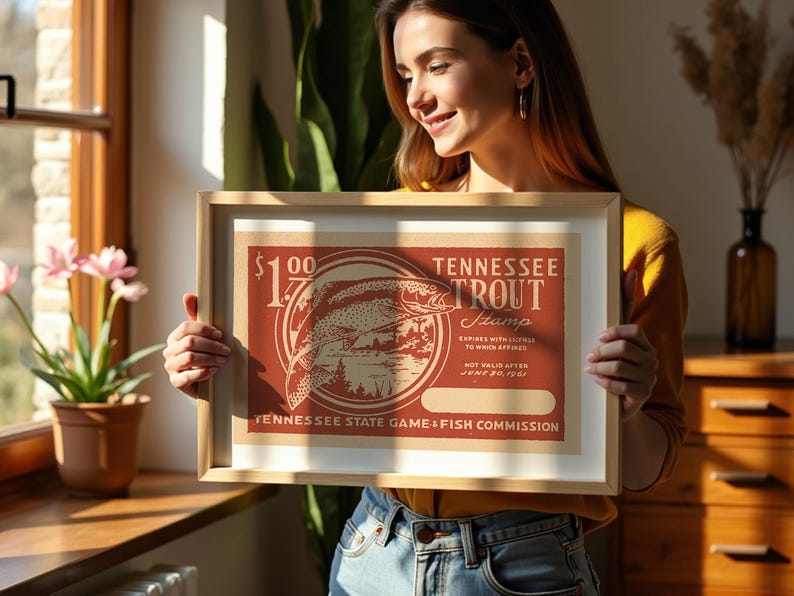 May include: Framed vintage Tennessee Trout Stamp art print. The print features a red and beige design with a trout illustration and text. The frame is a light wood colour.