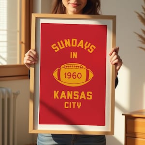 May include: A framed poster with a red background and yellow text. The text reads "Sundays in 1960 Kansas City". A yellow football is in the center of the poster.