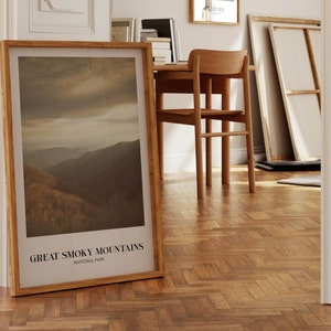 Op de afbeelding: Een ingelijste print van een berglandschap met de tekst "GREAT SMOKY MOUNTAINS NATIONAL PARK" onderaan. De print is in een houten lijst en leunt tegen een witte muur.