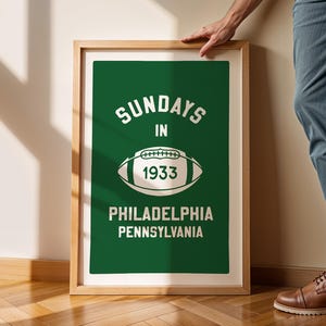 K&ouml;nnte beinhalten: Ein gerahmter Druck mit gr&uuml;nem Hintergrund und wei&szlig;em Text, der "Sundays in 1933 Philadelphia Pennsylvania" lautet. Eine wei&szlig;e Fu&szlig;ballgrafik ist mittig auf dem Druck platziert.