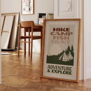 May include: A framed poster with a vintage design featuring a forest scene with two tents and the text "HIKE CAMP FISH HUNT ADVENTURE & EXPLORE".