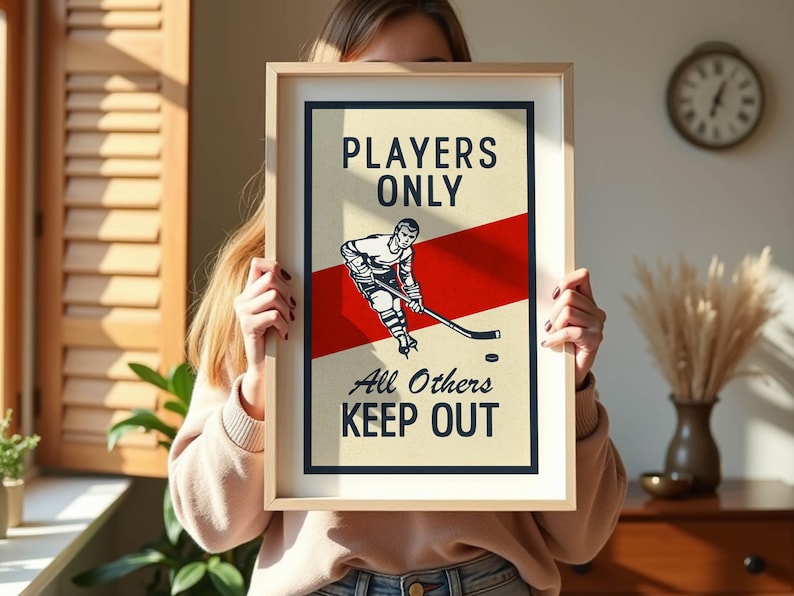 Pu&ograve; includere: Poster con cornice a tema hockey con un design vintage. Il poster presenta un'illustrazione di un giocatore di hockey, una striscia rossa e il testo "PLAYERS ONLY All Others KEEP OUT" in grassetto. Il poster &egrave; in una cornice di legno chiaro.