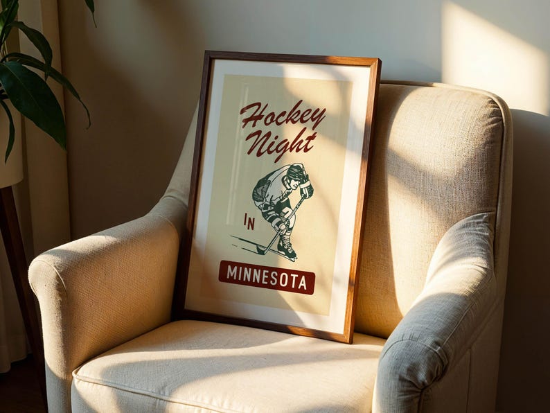 Puede incluir: Un p&oacute;ster enmarcado con un dise&ntilde;o vintage, que presenta una ilustraci&oacute;n de un jugador de hockey y las palabras "Hockey Night in Minnesota". El p&oacute;ster tiene un marco de madera marr&oacute;n y se exhibe en un sill&oacute;n beige.