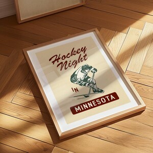 Puede incluir: P&oacute;ster enmarcado de estilo vintage con el texto "Hockey Night in Minnesota". La obra de arte presenta a un jugador de hockey en acci&oacute;n, en verde, blanco y negro. El p&oacute;ster est&aacute; sobre un fondo crema.