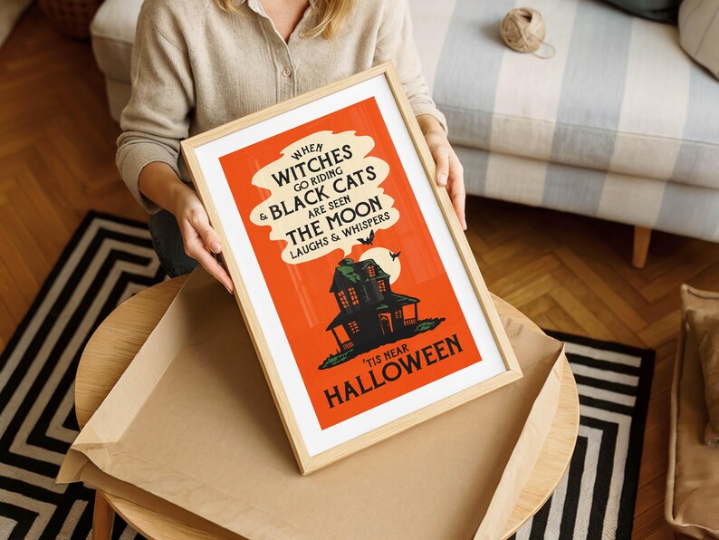 May include: A framed Halloween-themed poster with a vintage design. The poster features an orange background with black text and a haunted house illustration. The text reads "When witches go riding & black cats are seen, the moon laughs & whispers. 'Tis near Halloween."