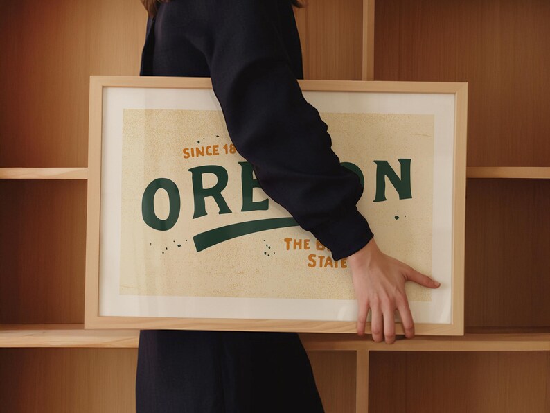 May include: A framed print with a vintage design featuring the word "OREGON" in green text with a green curved line underneath. The text "SINCE 1859" is above the word "OREGON" and the text "THE BEAVER STATE" is below the word "OREGON".