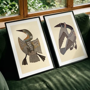 May include: Two framed art prints featuring stylized loon illustrations on a cream background. Each print is encased in a thin black frame, showcasing detailed bird figures with intricate patterns in shades of brown, gray, and white.