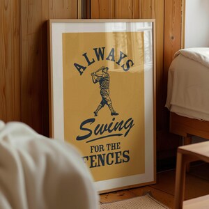 May include: Framed baseball-themed art print with a mustard yellow background. The print features a baseball player silhouette and the words "ALWAYS Swing FOR THE FENCES" in navy blue. The artwork is in a light wood frame.
