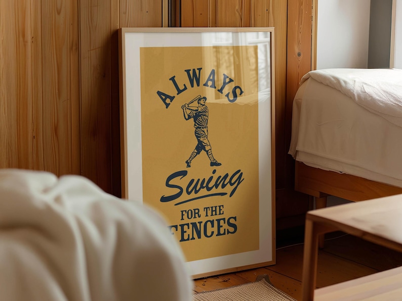 May include: Framed baseball-themed art print with a mustard yellow background. The print features a baseball player silhouette and the words "ALWAYS Swing FOR THE FENCES" in navy blue. The artwork is in a light wood frame.