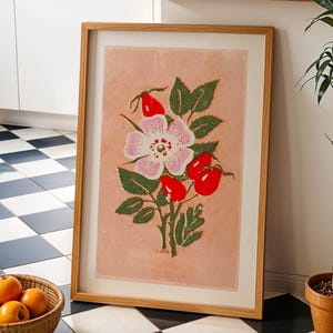 May include: A framed print of a pink and white flower with green leaves and red berries on a light pink background. The print is in a wooden frame.
