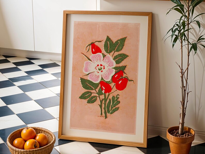 May include: A framed print of a pink and white flower with green leaves and red berries on a light pink background. The print is in a wooden frame.