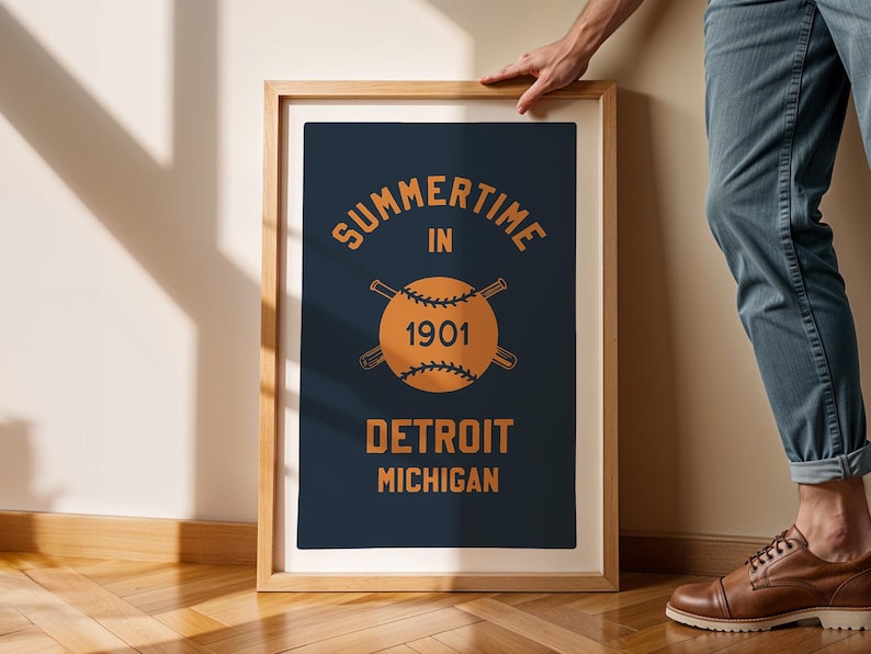 Peut inclure: Une impression encadr&eacute;e avec un fond bleu marine et un texte orange. Le texte indique "Summertime in 1901 Detroit Michigan". Une balle de baseball avec des chauves-souris crois&eacute;es se trouve au centre de l'impression.