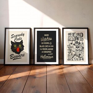 May include: Three framed Halloween-themed art prints. The first features a black cat with green eyes and the text "Scaredy Cats Beware." The second has the text "When Witches Go Riding." The third says "Oh My Cord It's Halloween."