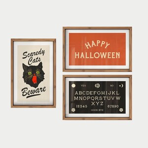 May include: Three framed Halloween-themed prints. One features a black cat with the text "Scaredy Cats Beware." Another has "Happy Halloween" on an orange background. The third is a Ouija board.