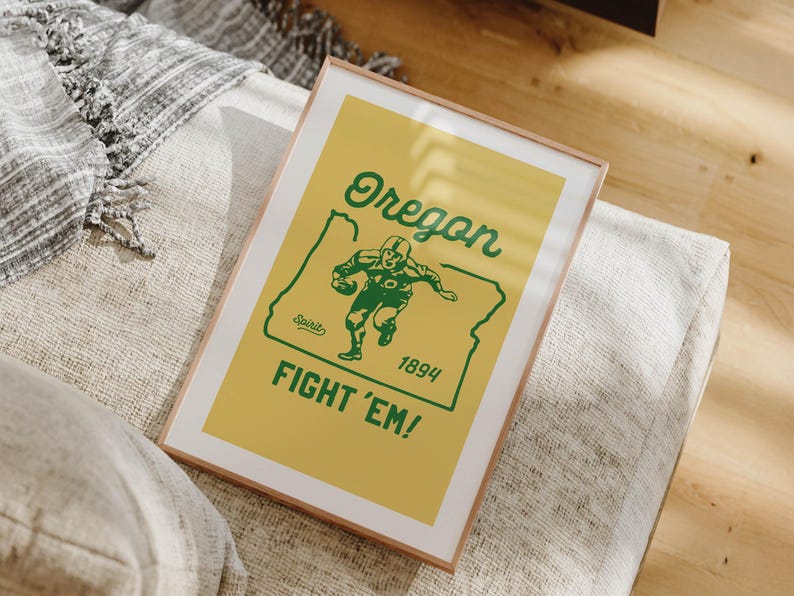 K&ouml;nnte beinhalten: Gerahmtes Poster mit gelbem Hintergrund und gr&uuml;nem Text und Grafiken. Der Text lautet "Oregon" &uuml;ber einer Grafik eines Footballspielers innerhalb der Umrisse des Staates. Unter der Grafik stehen die Worte "FIGHT 'EM!" und das Jahr "1894".