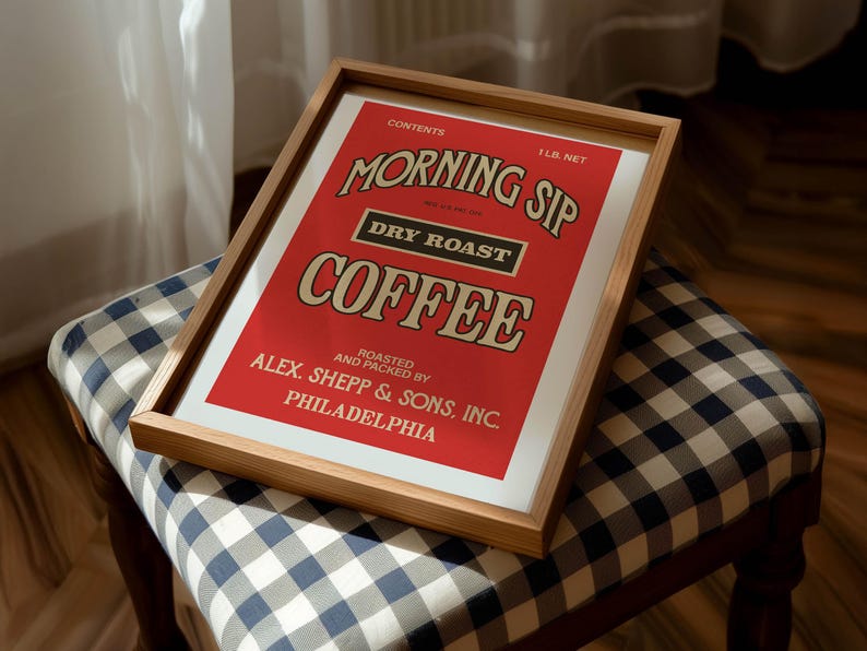 May include: A framed print with a red background, displaying the words "MORNING SIP COFFEE" in a vintage style. The print also includes the text "DRY ROAST" and "ALEX. SHEPP & SONS, INC PHILADELPHIA". The frame is made of light-coloured wood.