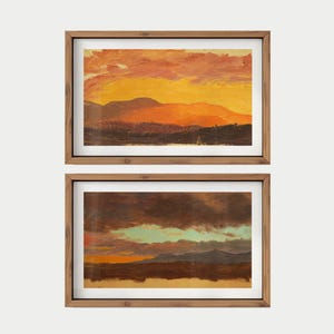 May include: Two framed landscape paintings. The top painting depicts a sunset with orange and yellow hues over mountains. The bottom painting shows a similar landscape with darker colors and a hint of blue sky. Both are in wooden frames.