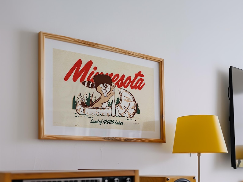 May include: A framed vintage poster with a cartoon illustration of a squirrel paddling a canoe. The poster is in a wooden frame and has the text "Minnesota Land of 10,000 Lakes".