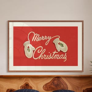 May include: A framed print with a red background and the words "Merry Christmas" in a cursive font. Two off-white mittens with holly accents are on the red background. The frame is a warm brown color.