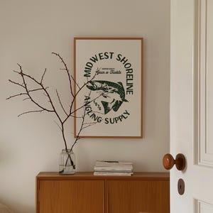 May include: A framed print with a white background and a green circle logo that says "Midwest Shoreline Angling Supply 1976 Gear & Tackle". The logo features a stylized image of a fish.