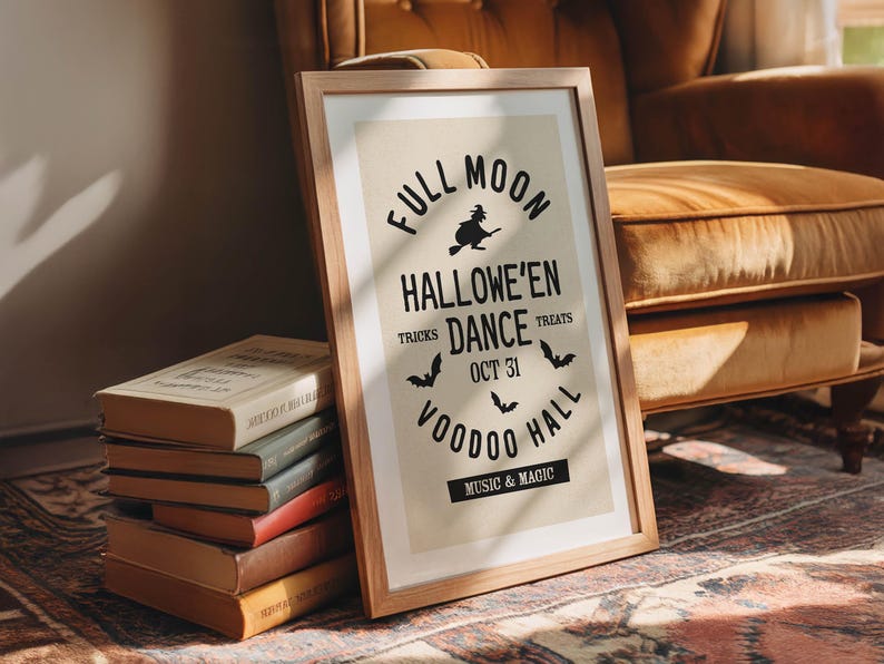 May include: A framed Halloween poster with a wooden frame. The poster features the text "Full Moon Hallowe'en Dance" with bats and a witch graphic. A stack of vintage books is in front of the poster.