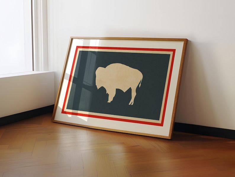 May include: A framed horizontal print featuring a cream-colored silhouette of a bison centered on a dark charcoal background. The artwork is enclosed by a thin red border and a wider cream-colored mat, all encased in a light wood frame.