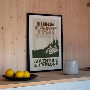 May include: A framed poster with a vintage design featuring the text "HIKE CAMP FISH HUNT ADVENTURE & EXPLORE" in brown and green lettering. The poster depicts a forest scene with two white tents.