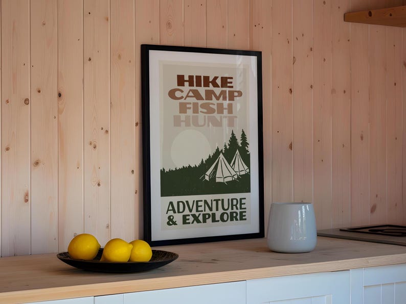 May include: A framed poster with a vintage design featuring the text "HIKE CAMP FISH HUNT ADVENTURE & EXPLORE" in brown and green lettering. The poster depicts a forest scene with two white tents.