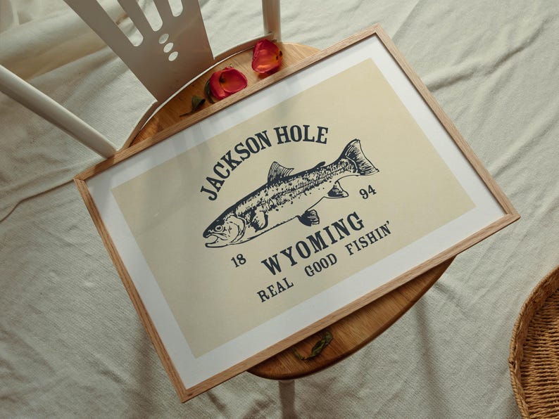 May include: A framed print featuring a detailed illustration of a fish, with text that reads "Jackson Hole Wyoming Real Good Fishin'". The print has a cream background and a wooden frame.