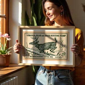 May include: Framed vintage Virginia Bear and Deer Hunting Stamp print. The artwork features a detailed illustration of a deer leaping over a log. The text reads "Virginia Bear and Deer Hunting Stamp" and "Nonresident 1945-46".