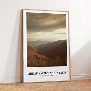 Op de afbeelding: Een ingelijste print van een schilderachtig uitzicht op het Great Smoky Mountains National Park. De afbeelding toont een mistig, goudkleurig landschap met glooiende heuvels en een bewolkte lucht.