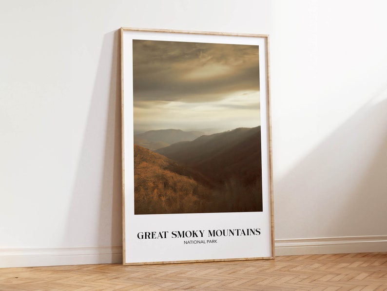 Op de afbeelding: Een ingelijste print van een schilderachtig uitzicht op het Great Smoky Mountains National Park. De afbeelding toont een mistig, goudkleurig landschap met glooiende heuvels en een bewolkte lucht.