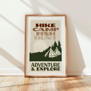 May include: A framed print with a vintage aesthetic featuring the text "HIKE CAMP FISH HUNT ADVENTURE & EXPLORE" in brown and white lettering. The print depicts a forest scene with two tents and a sun in the background.