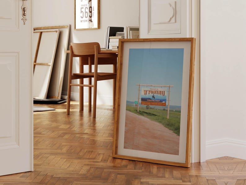 May include: A framed photograph of a scenic road leading to a sign that reads "Welcome to Wyoming, The Equality State" with a cowboy riding a horse in the background.