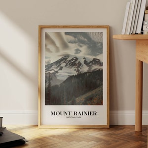 K&ouml;nnte beinhalten: Ein gerahmtes Poster mit einem Foto vom Mount Rainier National Park. Das Bild zeigt einen schneebedeckten Berggipfel mit Wolken am Himmel. Der Text "MOUNT RAINIER NATIONAL PARK" ist unter dem Bild gedruckt.