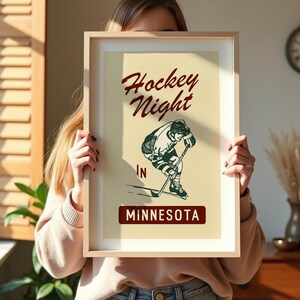 Puede incluir: P&oacute;ster enmarcado con una ilustraci&oacute;n de hockey de estilo vintage. El p&oacute;ster presenta el texto "Hockey Night" en escritura burdeos sobre un gr&aacute;fico de jugador de hockey verde y blanco. Debajo, el texto "IN MINNESOTA" se muestra en un rect&aacute;ngulo burdeos.